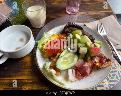Hotel buffet breakfast in Rome, Italy. Plate with kiwi, scrambled eggs, cold cuts, and quiche served on patterned placemat. Stock Photo