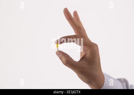 Fingers holding a yellow capsule close up Stock Photo