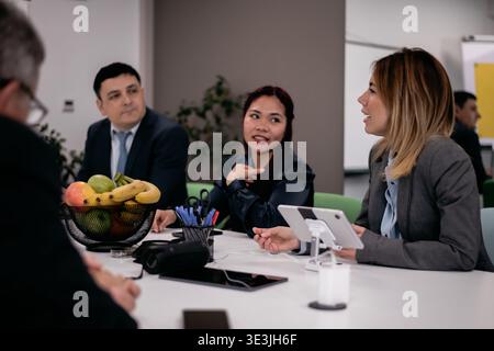 Business professionals engage in a collaborative meeting around a table with documents and fruit Stock Photo