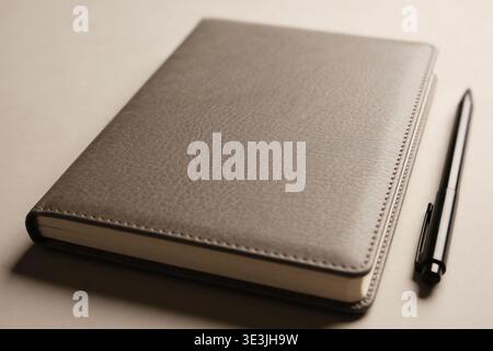 A close-up view of a sophisticated gray journal with a textured cover, placed next to a modern black pen, suggesting organization and planning Stock Photo