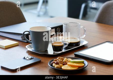 A modern office desk setup featuring coffee cups, a mix of nuts and citrus slices, a smartphone, and a tablet, perfect for a business break Stock Photo