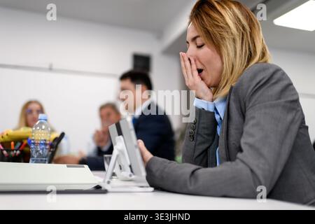 Meeting takes place in an office with several people in attendance as one person yawns during the discussion while wearing a business suit Stock Photo