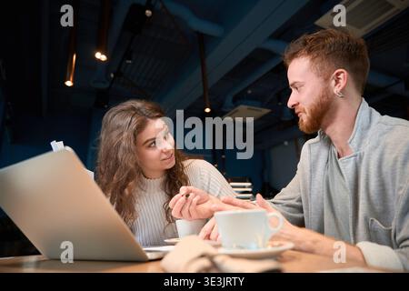Young adults collaborating over laptop in coffee shop Stock Photo