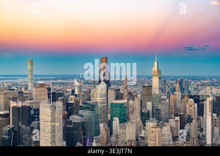 A high angle aerial view shows the dense skyline of Midtown Manhattan under a vibrant pink and orange sunset sky in New York. Stock Photo