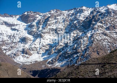 Expansive view of snow-covered Atlas Mountains rising above the rugged Moroccan highlands, showcasing rocky peaks, alpine textures and clear blue skie Stock Photo
