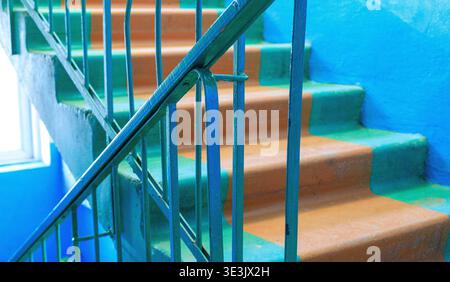 Old apartment building staircase with worn concrete steps and turquoise metal railings. Authentic vintage interior, distressed textures. Renovation co Stock Photo