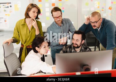 Business team collaborates on a project while reviewing data on a computer screen in a modern office setting Stock Photo