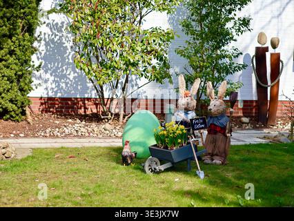 A front yard decorated for Easter featuring large straw bunny figures, a giant green egg, and a sign saying Frohe Ostern Happy Easter Stock Photo