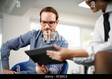 Business professionals discussing strategies during a meeting in a modern office space with a focus on digital tools and technology Stock Photo