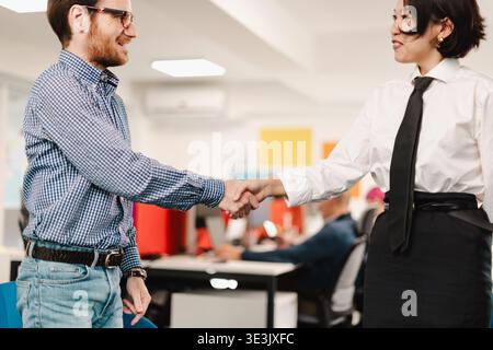 Business meeting showing handshake between two professionals in a modern office setting during daytime with colleagues engaged in work Stock Photo