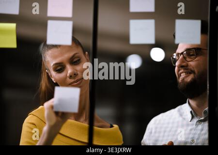 Team members collaborate on brainstorming session with sticky notes in modern office environment during evening hours Stock Photo