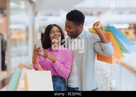 Couple Enjoys a Fun Shopping Day at the Mall While Using Their Smartphone Together Stock Photo