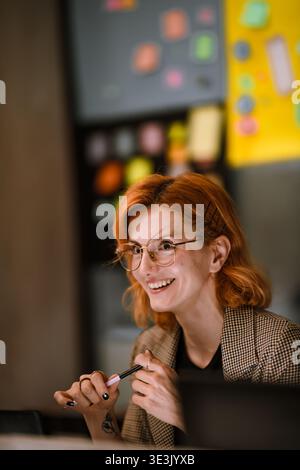 Smiling woman in glasses engages in discussion during creative brainstorming session at modern workspace filled with colorful sticky notes Stock Photo