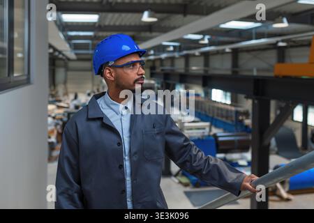 An African American male engineer observes the production line while using technology in a modern industrial setting. Stock Photo