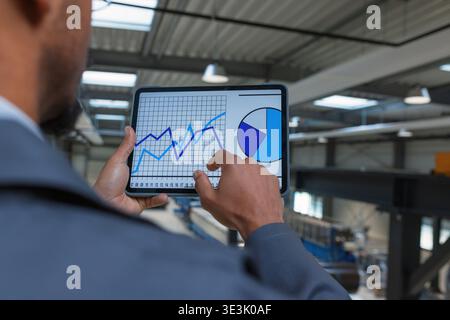An African American male engineer checks production data on a tablet while overseeing operations in an industrial setting. Stock Photo
