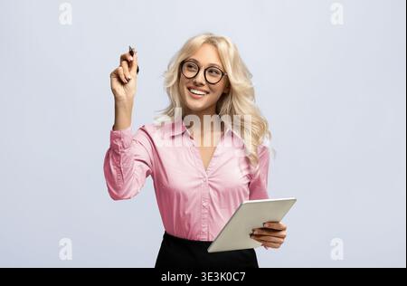 Young Woman Holds a Tablet and Smiles While Thinking of Ideas in a Light Setting Stock Photo