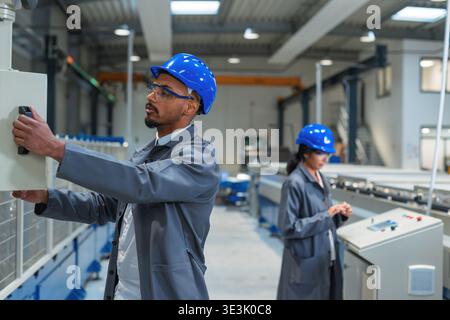A team of engineers works together in a factory setting, focusing on production tasks and using modern technology for efficiency. Stock Photo