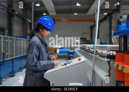 An Indian female engineer is working on machinery in an industrial factory, wearing safety gear and focused on her task. Stock Photo