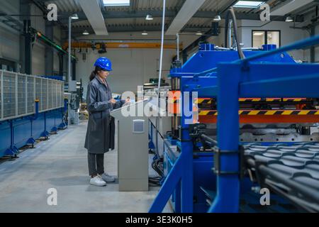An Indian female engineer works on machinery in a factory while wearing safety gear. She is focused on her task at a production line. Stock Photo