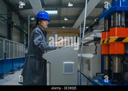 An Indian female engineer works in a factory while wearing safety gear and operating machinery. Stock Photo