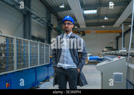A male engineer in a safety helmet stands in an industrial facility while using technology to monitor production lines. Stock Photo