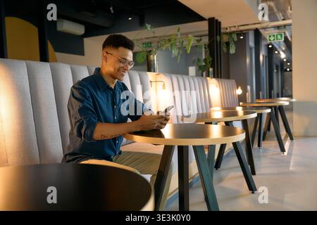 Confident young businessman using smartphone while sitting in office lounge during evening Stock Photo