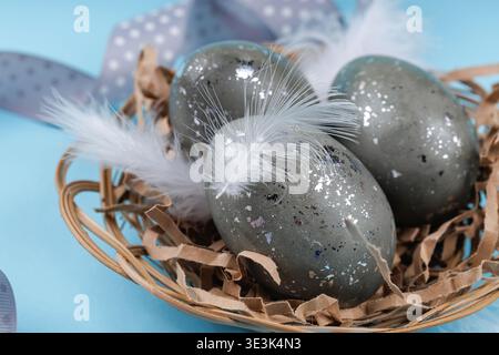 Close up Easter eggs with feathers in nest on blue background Stock Photo
