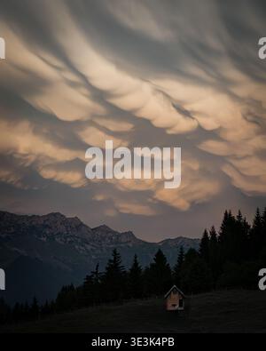 A small cabin in the mountains beneath dramatic mammatus clouds during sunset. Stock Photo