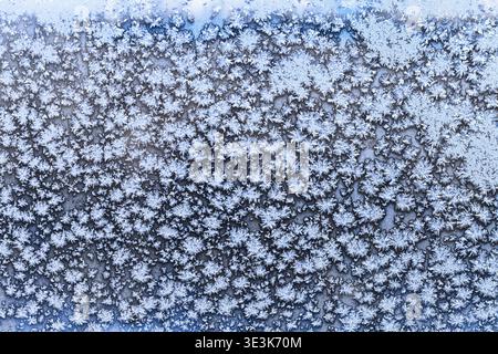Snowflakes and frost patterns on frozen window panes on cold winter evenings Stock Photo