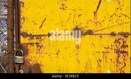 Rusty yellow metal gate with padlock and scratched industrial surface Stock Photo