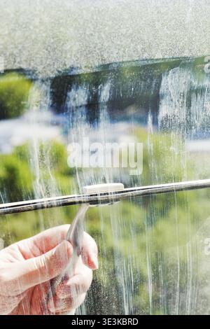 Cleaning the house window pane with a squeegee on a sunny spring day Stock Photo