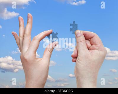 Male and female hands holding small puzzle pieces with blue sky background Stock Photo
