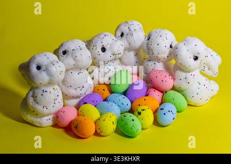 White glitter Easter bunnies and colorful speckled eggs on a bright yellow background. Spring holiday decoration and celebration concept. Stock Photo