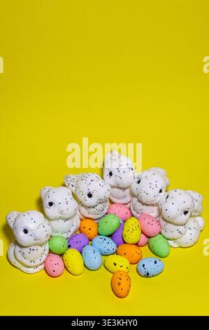 White glitter Easter bunnies and colorful speckled eggs on a bright yellow background. Spring holiday decoration and celebration concept. Stock Photo