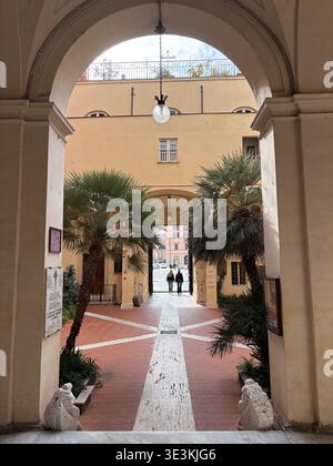 Basilica San Silvestro in Capite courtyard, Rome, Italy. View through arcaded cloister showing palm trees and two people exiting. Stock Photo