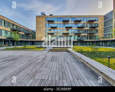 A modern residential courtyard featuring weathered wooden decking in the foreground, surrounded by contemporary multi-story apartment buildings with Stock Photo