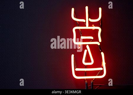 A close-up photograph of a glowing red neon sign mounted on a dark textured wall. The neon tubing forms two Chinese characters, 'å‡ºå›½' (chÅ« guÃ³), which Stock Photo