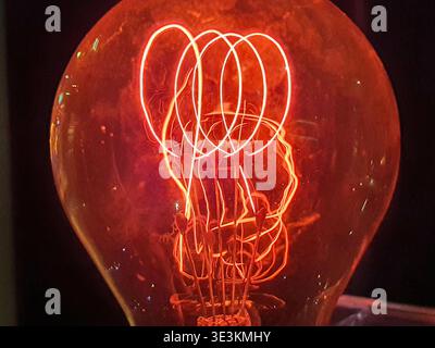 Close-up macro photograph of a vintage incandescent light bulb with an intricate glowing filament. The tungsten wire forms multiple bright orange-red Stock Photo