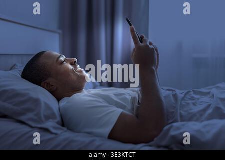 Young black man lying in bed at night using smartphone Stock Photo