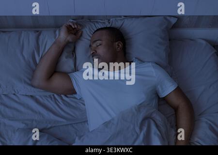 Young african american man sleeping in bed at night under blanket Stock Photo