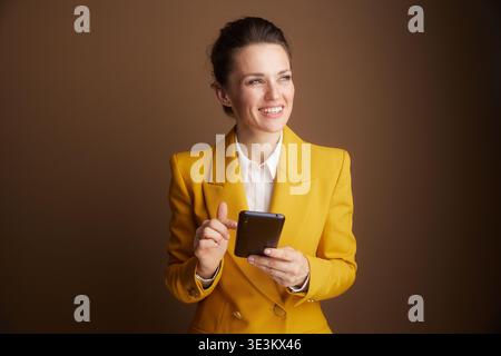 A professional woman in a yellow blazer intently interacts with a smartphone, showcasing digital engagement and modern communication within a business Stock Photo