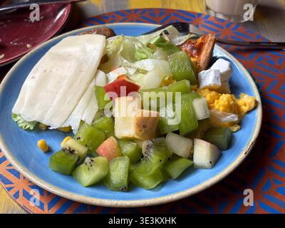 Hotel buffet breakfast selection in Rome, Italy, featuring fresh kiwi fruit salad, sliced cheese, scrambled eggs, and a small quiche slice. Stock Photo