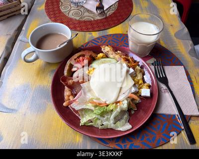 Hotel buffet breakfastl in Rome Italy featuring cheese slices, bacon, salad, and milk beverage on rustic table. Stock Photo