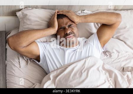 Young black man lying in bed holding head in pain, having headache Stock Photo