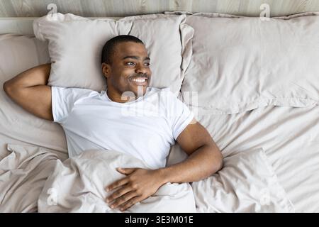 Black man lying in bed smiling and relaxed, looking away, representing comfort Stock Photo