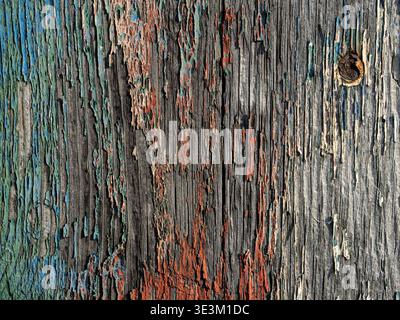 Close-up of heavily weathered wooden boards with peeling teal + red paint creating a rustic textured background. Stock Photo