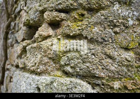 Close-up of ancient weathered stone wall texture with green moss and rough surface Stock Photo