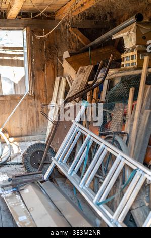 Messy old workshop interior with tools ladder and wheelbarrow, rustic workspace, concept of manual work, repair, maintenance and authentic rural lifes Stock Photo