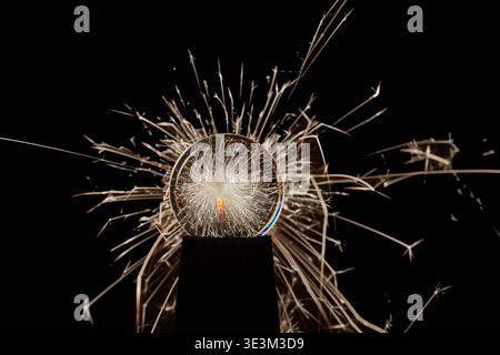 Burning sparkler behind a glass ball on a black background. Stock Photo