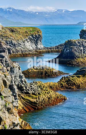 Visitors can see the unique rock formations along the coastline at Arnarstapi in Iceland during a sunny day by the water. Stock Photo